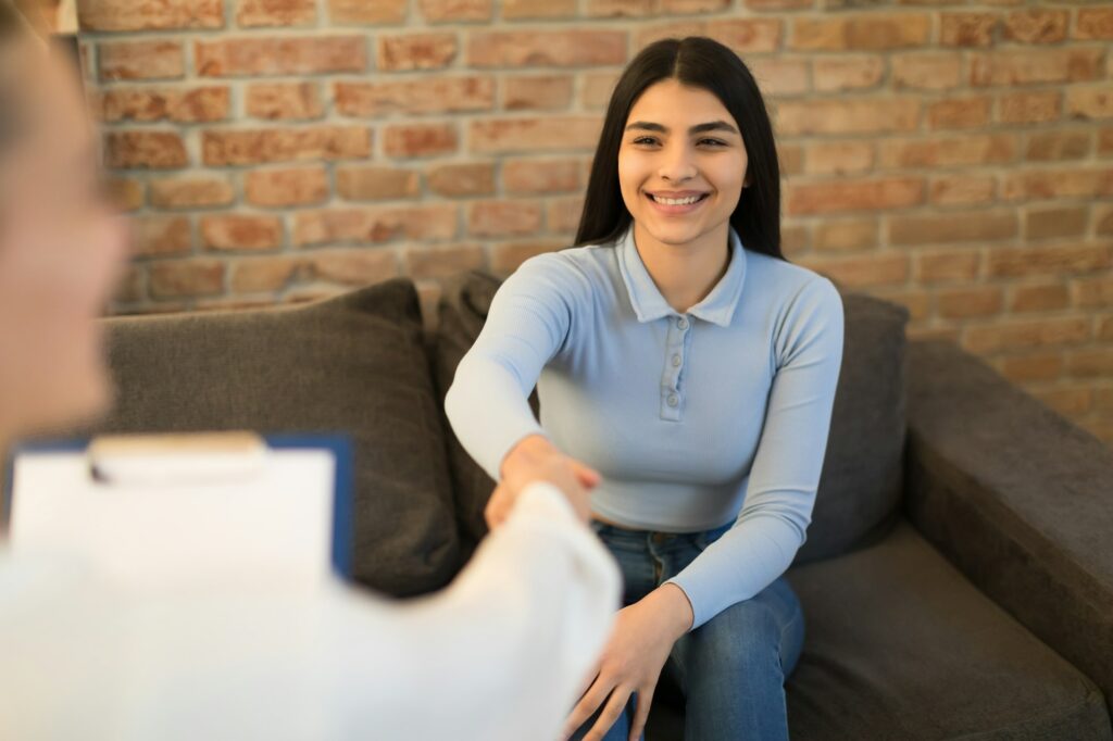 Happy teenage girl visiting psychotherapist and shaking hands during the session in office